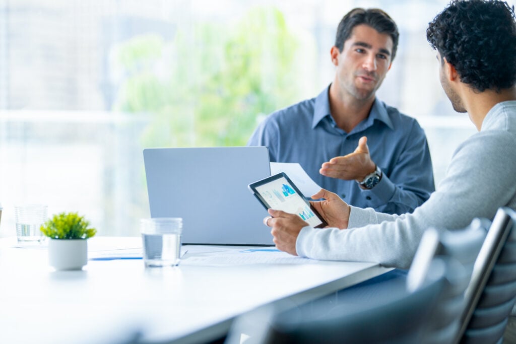 Two businessmen working on a digital tablet and laptop computer in the office.