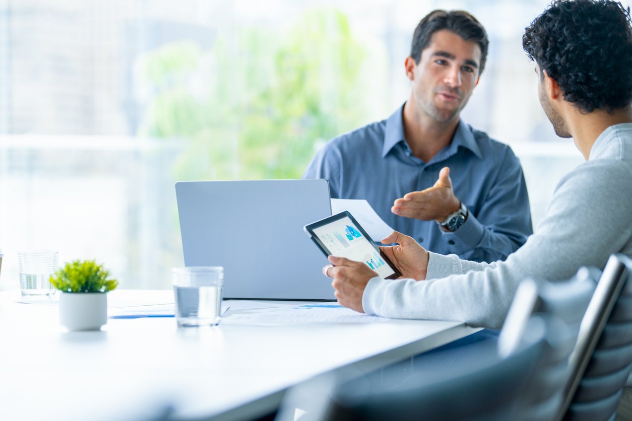 Two businessmen working on a digital tablet and laptop computer in the office.